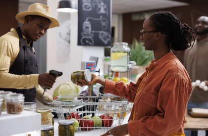 Male shopkeeper of an eco friendly store promotes sustainable shopping and provides fresh, organic, and plastic-free items. A side0view shot of a black cashier scanning products at the counter.